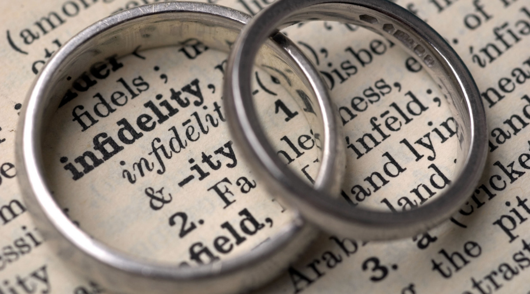 Two silver rings overlapping on top of dictionary entry on "infidelity"