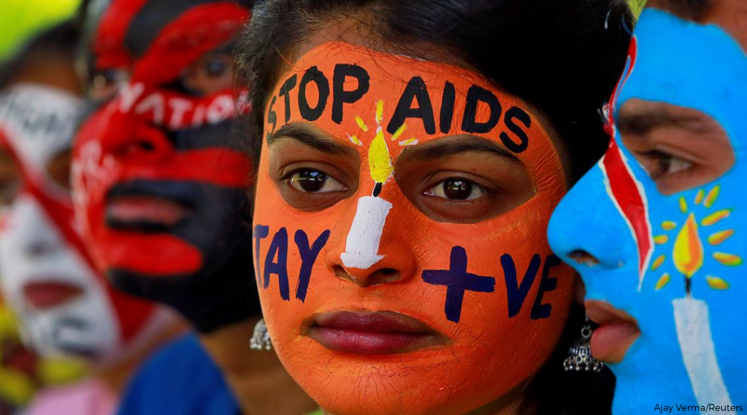 Indian woman's face painted in orange written with "Stop AIDS" in black paint across forehead