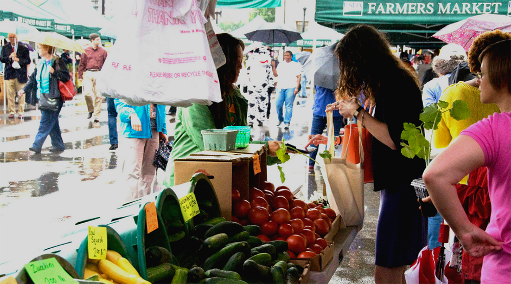 USDA farmer's market with a table of zucchini and a female shopper looking over