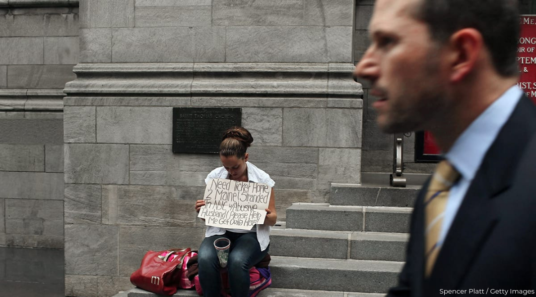 Woman sitting on stone steps and holding up sign asking for money to travel and white businessman passing by