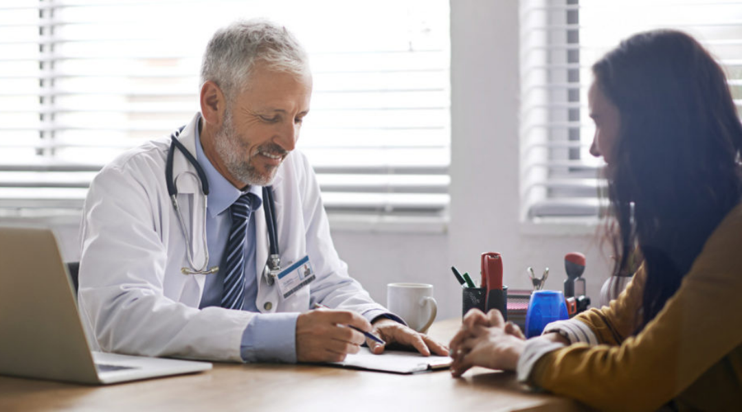 white male physician with young adult female patient, both smiling