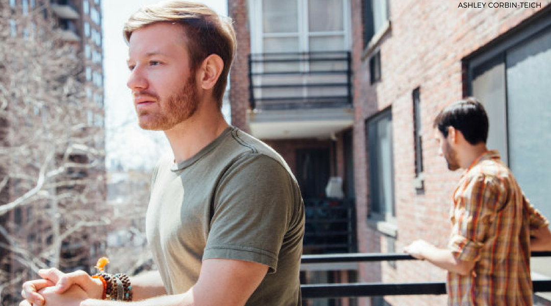 Young, gay white couple with partners looking out on balcony in different directions