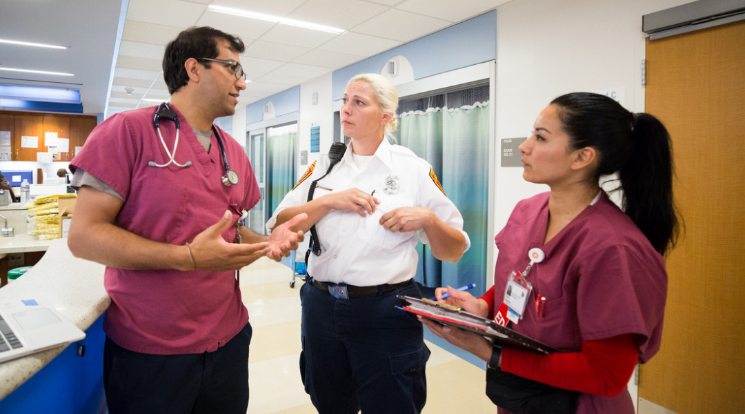 A doctor, EMT and nurse sharing a discussion in a hospital setting. 