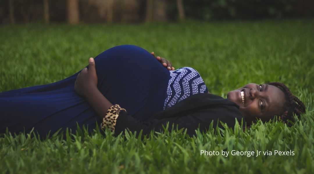 A pregnant woman laying down in a grass field. 