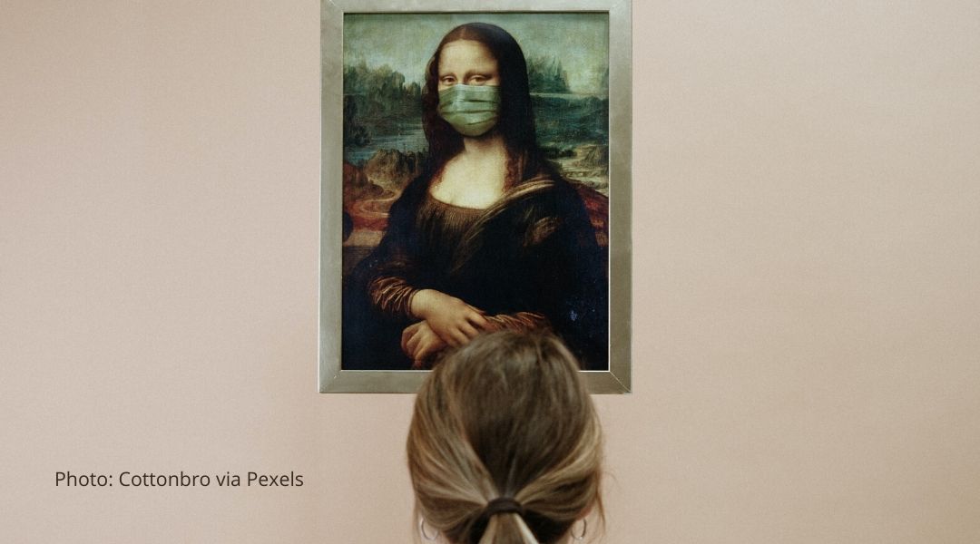 A woman studies a painting of the mona lisa who is wearing a protective mask