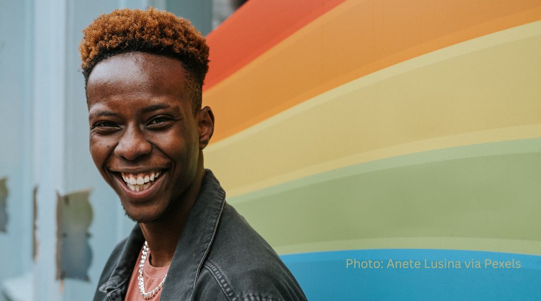 A young man stands in front of a rainbow mural